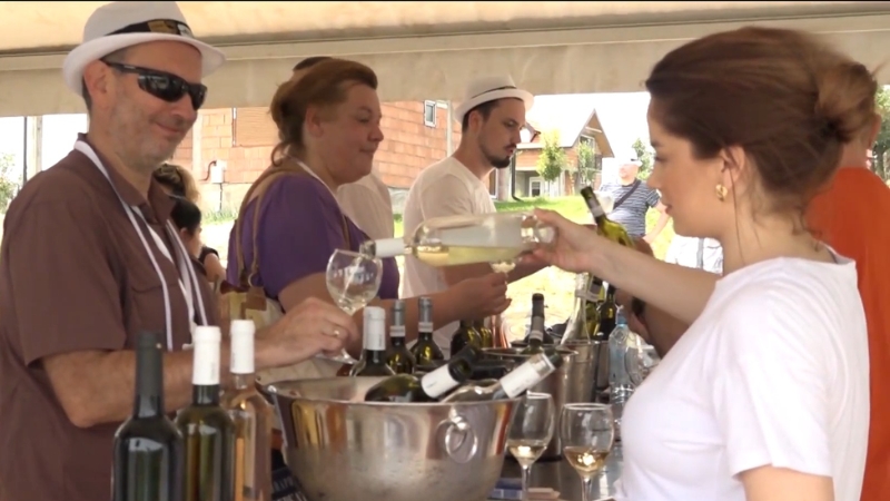 Prodavac sipa belo vino posetiocu za štandom tokom vinskog festivala na otvorenom